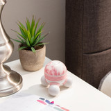 Pink | Pink Homedics Marbelous Mini Massager sitting on a table with lamp, plants, and books