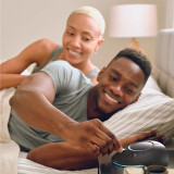 Night | Homedics Portable Sound Machine with Night Light placed on a bedside table, while a couple relaxes in bed