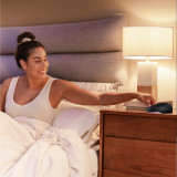 Night | Homedics Portable Sound Machine with Night Light placed on a bedside table, while a woman relaxes in bed.